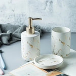 White marble-pattern bathroom accessory set with gold veining, including a soap dispenser with a gold pump, a tumbler cup, and a matching soap dish on a countertop.