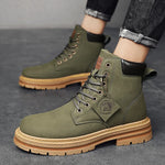 A pair of sleek black leather ankle boots with rugged rubber soles, lace-up fronts, and metal eyelets, displayed on a gray fabric surface with one boot propped up on a vintage-style book for presentation.