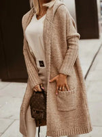 Person wearing a long beige cardigan over a white top, holding a brown bag.