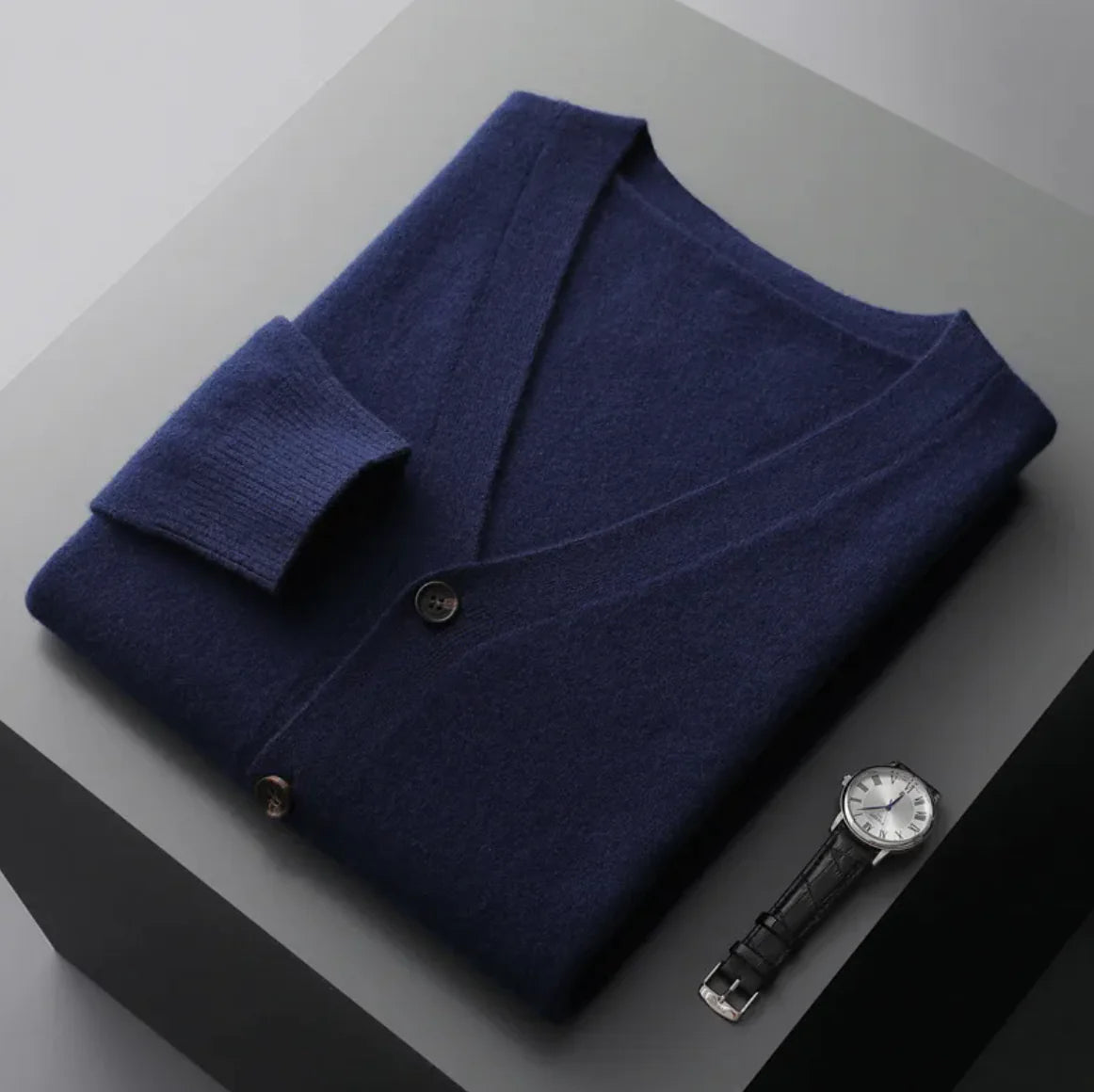 A neatly fold shirt on a black surface with a black wrist watch near it