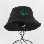 Black bucket hat with a green leaf embroidery on the front, displayed on a wire stand against a white background.