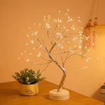 Warm white LED “tree” lamp with many tiny lights on silver branches, mounted on a small round base, sitting on a tabletop next to a small potted plant in a softly lit room.
