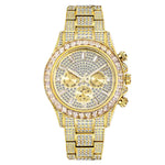 A product photo of a gold-tone wristwatch heavily decorated with clear rhinestones/crystals across the bracelet links and the entire dial. The round face has a crystal-studded bezel, three sub-dials (chronograph-style), and three pushers/crown on the right side. The overall look is flashy “iced-out” jewelry style on a white background.
