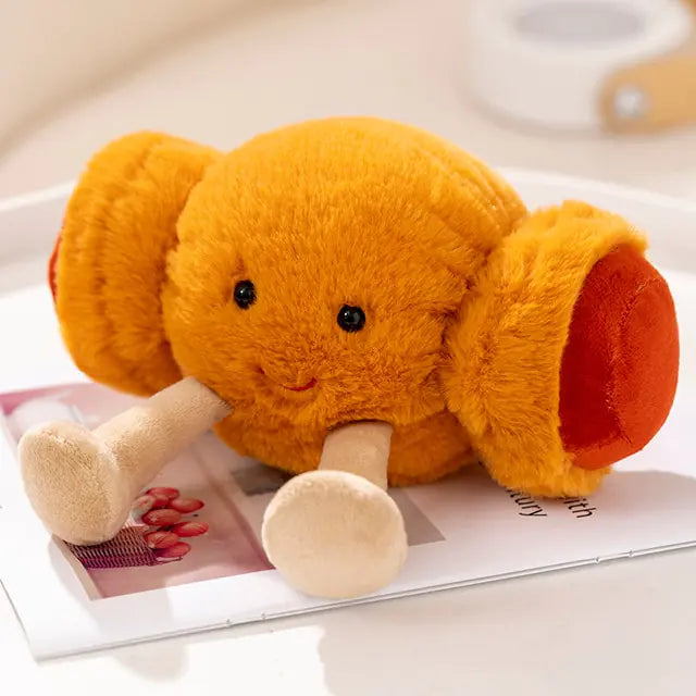 A cute orange plush crab with a smiling face, small black eyes, and a pair of soft legs, sitting on a magazine.