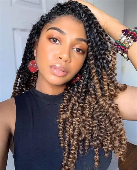 Woman taking a selfie with long chunky twist braids in a dark-to-honey-brown ombré, wearing a black sleeveless top, red earrings, and stacked bracelets, with one hand in her hair.