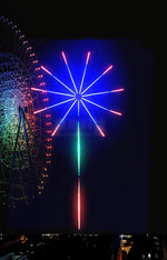 Colourful firework-style LED light display with red, blue and green glowing strips against a dark night background.
