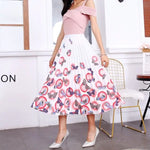 Pleated midi skirt with a gradient design, transitioning from dark black at the waistband to a soft blush pink at the hem, hanging on a black clothing rack next to a vintage-style camera.