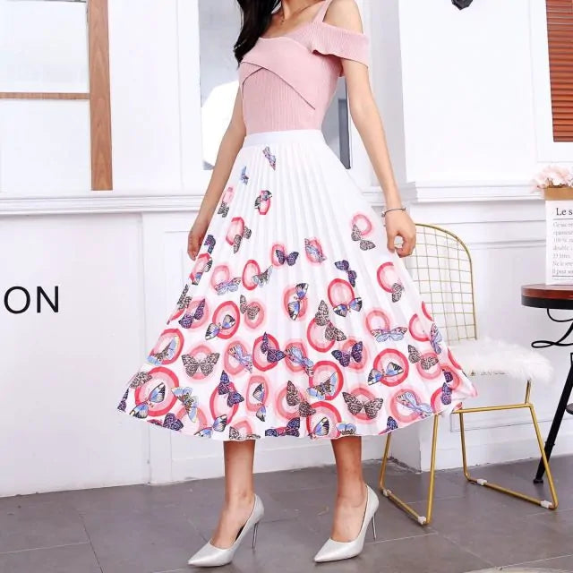 Pleated midi skirt with a gradient design, transitioning from dark black at the waistband to a soft blush pink at the hem, hanging on a black clothing rack next to a vintage-style camera.
