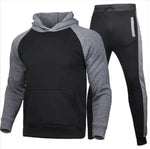 A stylish two-piece men's tracksuit. The set includes a hooded sweatshirt with a kangaroo pocket and long gray sleeves, along with matching jogger pants that have a drawstring waist and gray side panels with zippered pockets. The design offers a sporty yet casual look, ideal for workouts or everyday wear.