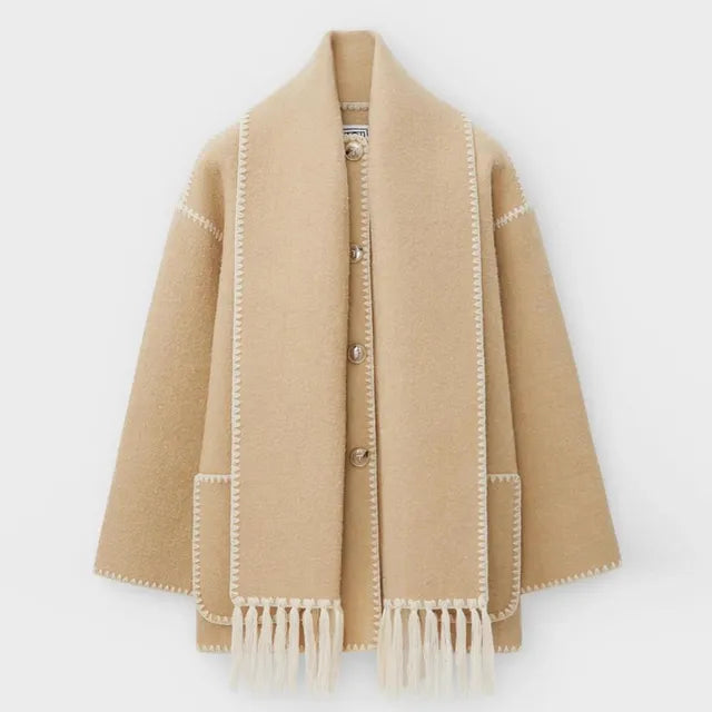 Dark wool coat with white blanket stitch trim, featuring front buttons, large patch pockets, and an attached matching scarf with fringe detailing draped over the shoulder. The coat is displayed against a plain white background.
