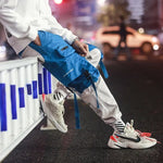 Blue and grey cargo joggers with utility pockets, buckle straps and drawstring details.
