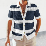 Man wearing a short-sleeve knit button-up shirt with navy-and-white horizontal stripes, a white collar and sleeve cuffs, and large front buttons, paired with light-colored trousers.