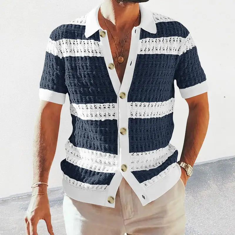 Man wearing a short-sleeve knit button-up shirt with navy-and-white horizontal stripes, a white collar and sleeve cuffs, and large front buttons, paired with light-colored trousers.