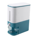 White-and-teal automatic dispenser with a side viewing window, a front knob, and a clear measuring cup attached at the bottom for dispensing dry food or grains.