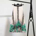 Pleated midi skirt with a gradient design, transitioning from dark black at the waistband to a soft blush pink at the hem, hanging on a black clothing rack next to a vintage-style camera.