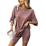 Woman wearing a matching ribbed mauve loungewear set consisting of a loose-fitting oversized top and fitted shorts, accessorized with a crossbody bag, bracelet, and holding a white takeaway coffee cup.