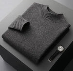 A neatly folded beige knitted sweater with a ribbed high collar and cuffs, placed on a dark grey surface. Beside the sweater, a classic wristwatch with a black leather strap and a silver dial is positioned, adding a touch of elegance to the composition.
