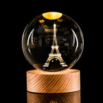 Crystal ball lamp with a laser-etched Eiffel Tower inside, glowing warm light on a wooden base against a black background.
