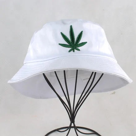 White bucket hat with an embroidered green leaf emblem on the front, displayed on a metal stand against a light background.