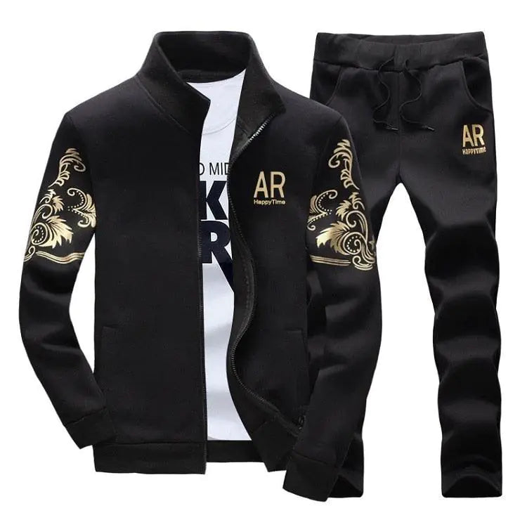 Black men’s tracksuit set on a white background: zip-up jacket and matching joggers with gold “AR” logo and gold ornamental swirl designs on the sleeves and upper thighs, shown over a white T-shirt.