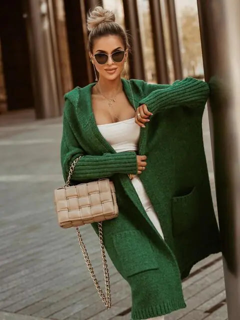 Woman wearing a green cardigan over a white top, holding a beige handbag.