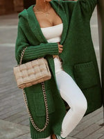 Person wearing a green cardigan, white top, and pants, holding a beige woven handbag.