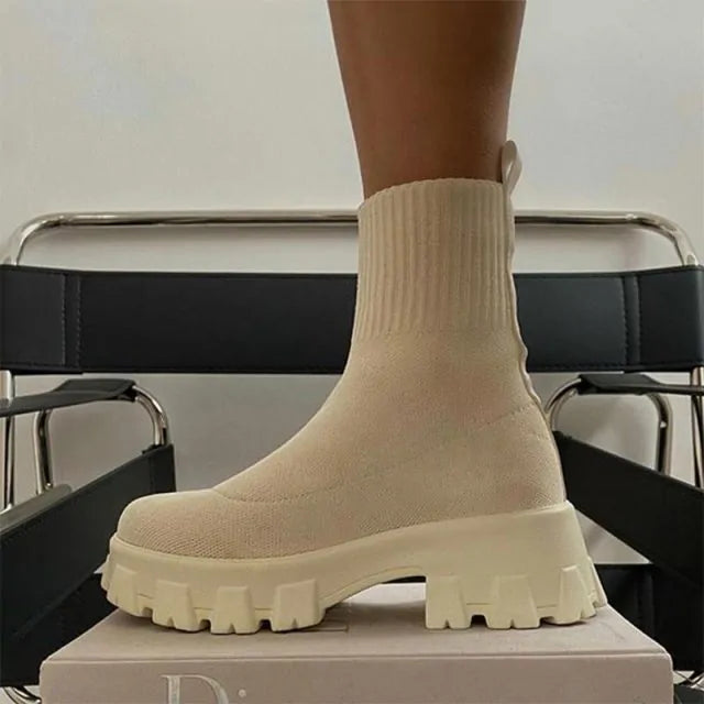 A pair of chunky lavender sock boots with thick platform soles and ribbed knit uppers, displayed on a gray tiled floor against a light-colored wall.