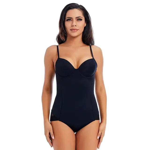 A studio product photo of a woman modeling a black one-piece shapewear bodysuit on a white background. The garment has thin shoulder straps, a molded bra/cup top with a deep sweetheart neckline, and a smooth, fitted midsection with brief-style bottoms.