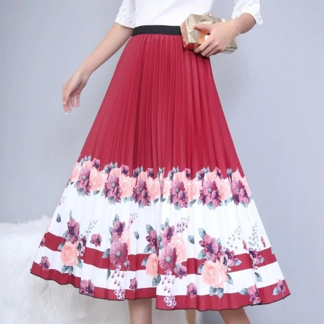 Pleated midi skirt with a gradient design, transitioning from dark black at the waistband to a soft blush pink at the hem, hanging on a black clothing rack next to a vintage-style camera.