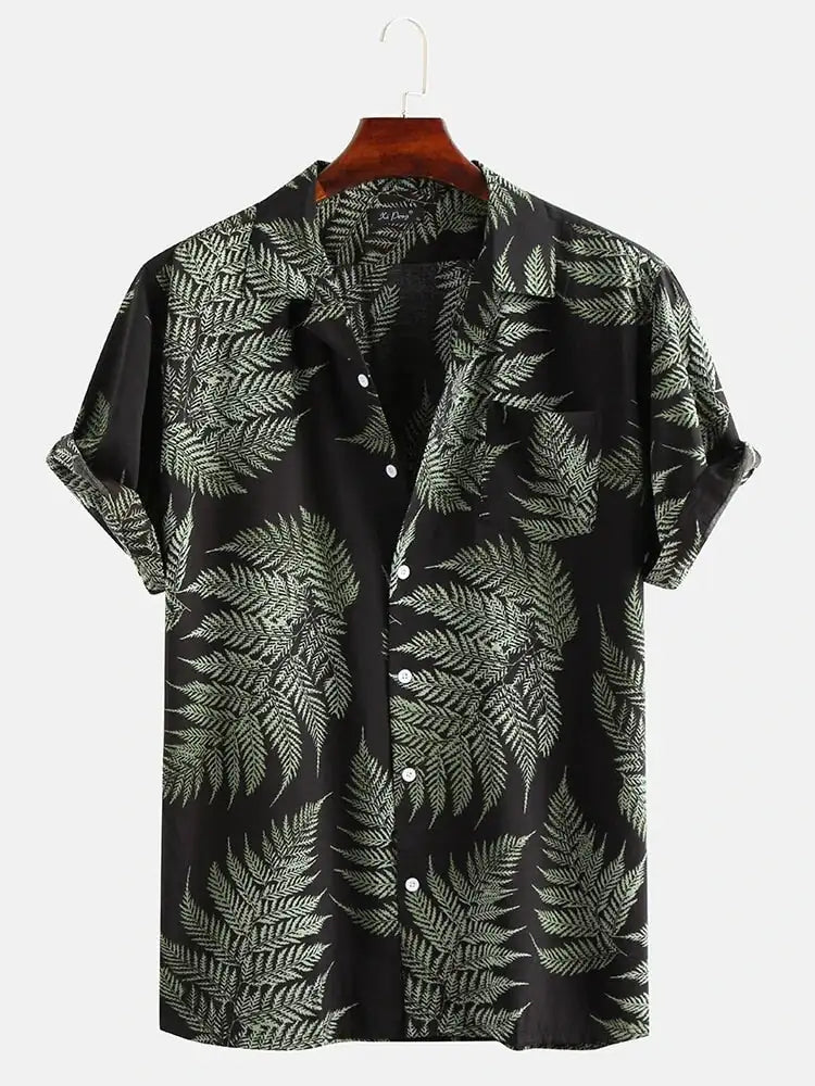 A studio product image of a black short-sleeve button-up shirt on a hanger, featuring an all-over green fern/leaf print, a spread collar, rolled sleeve cuffs, and white buttons, photographed against a light background.