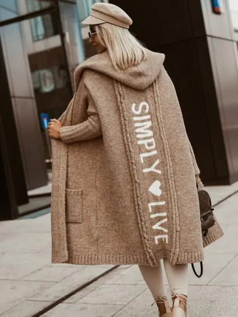 Person wearing a long beige coat with 'Simply Live' text, standing on a city street.