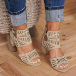 A close-up view of a person wearing stylish beige cut-out heeled sandals with ankle straps and decorative perforations, paired with cuffed blue denim jeans on a wooden floor.