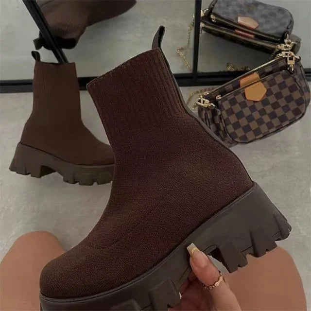 A pair of chunky lavender sock boots with thick platform soles and ribbed knit uppers, displayed on a gray tiled floor against a light-colored wall.