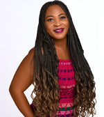 Smiling woman with long, braided hair and an ombre effect, wearing a colorful pink dress.