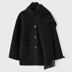 Dark wool coat with white blanket stitch trim, featuring front buttons, large patch pockets, and an attached matching scarf with fringe detailing draped over the shoulder. The coat is displayed against a plain white background.