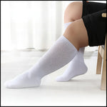A pair of sleek, white over-the-knee stiletto boots with pointed toes and side zippers, featuring decorative buckles at the top, worn in a modern, minimalist room with textured white wall panels.