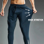 A muscular man wearing dark athletic joggers demonstrates the high-stretch capability of the fabric by pulling the side of the pants outward. The image has a dark gradient background, and bold white text that reads "HIGH STRETCH" with three arrows pointing to the stretched fabric, emphasizing its elasticity. The joggers feature an elastic waistband with a drawstring and a sleek, tapered fit, ideal for sports and activewear.