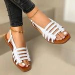 White strappy flat sandals worn with dark skinny jeans and ankle bracelets.