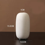 Small ribbed white ceramic vase on a dark surface against a brown background, labeled with dimensions: 15.5 cm tall, 9.5 cm wide at the base, and a 1 cm opening at the top.