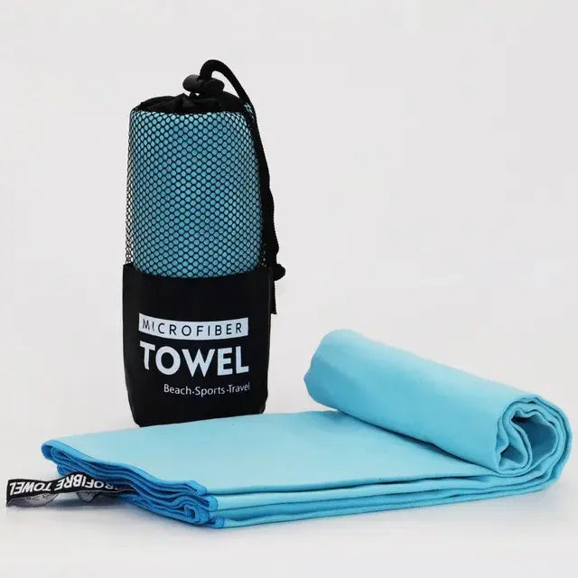 Light blue microfiber towel rolled and folded beside a black mesh drawstring pouch labeled “MICROFIBER TOWEL,” on a white background.