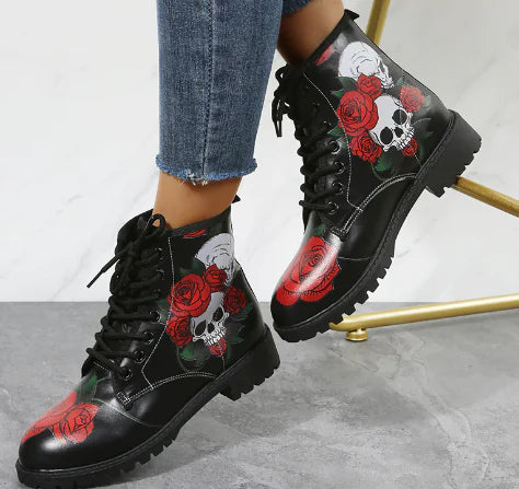 Black combat boots with skull and rose designs worn with blue jeans on a light gray background.