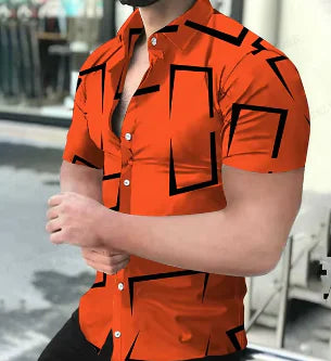 A muscular man wearing a stylish short-sleeved button-up shirt. The upper part of the shirt is purple with a geometric pattern resembling a honeycomb, while the lower part is solid black. The shirt is partially unbuttoned, revealing part of his chest. The background appears to be an outdoor urban setting with blurred reflections in a glass window and some chairs visible.