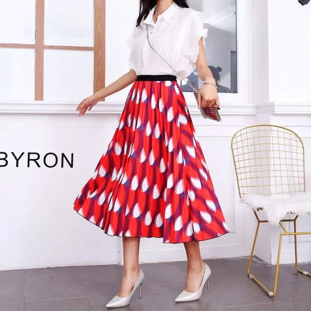 Pleated midi skirt with a gradient design, transitioning from dark black at the waistband to a soft blush pink at the hem, hanging on a black clothing rack next to a vintage-style camera.