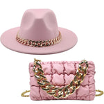 A coordinated pink accessories set featuring a soft wide-brim hat and a ruched rectangular handbag. Both pieces are accented with chunky gold chain details, and the set is displayed against a plain light gray background.