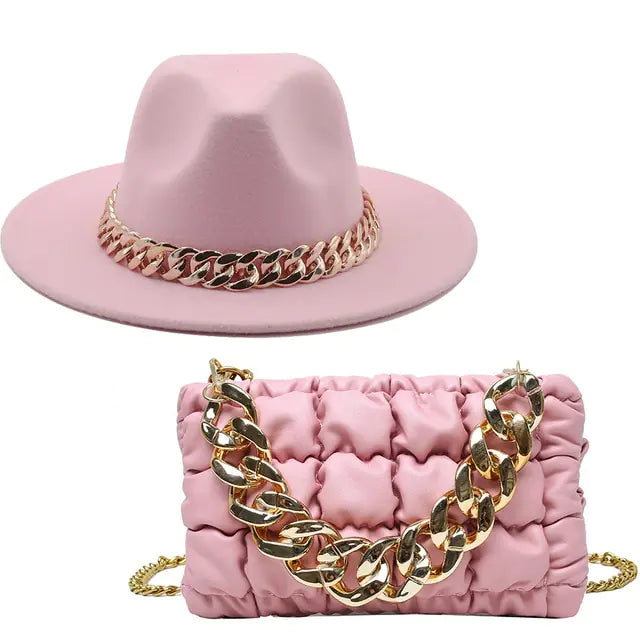 A coordinated pink accessories set featuring a soft wide-brim hat and a ruched rectangular handbag. Both pieces are accented with chunky gold chain details, and the set is displayed against a plain light gray background.