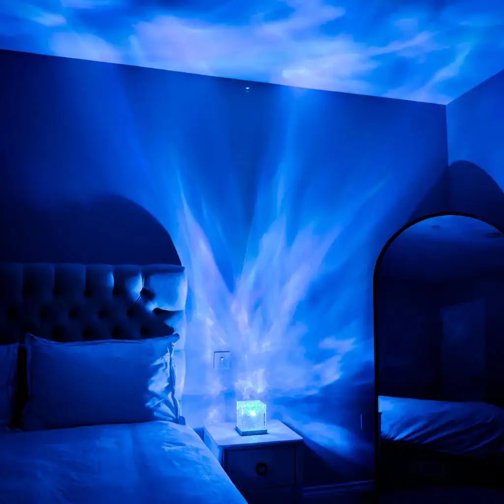 Dim bedroom lit in blue, with an ocean/wave-style light projector casting moving water patterns onto the walls and ceiling above a bed and nightstand.