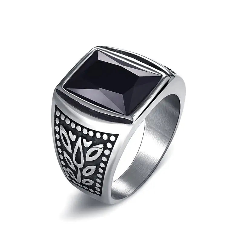 Silver signet-style ring with a large square black faceted stone on top and an engraved leaf motif on the side, shown on a white background.