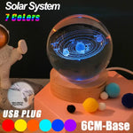 The image shows a 3D LED lamp that displays a holographic representation of the solar system. The planets orbit the sun within a glass globe, with the lamp base made of wood. It also features a USB plug for powering the light and comes with seven color options for illumination.