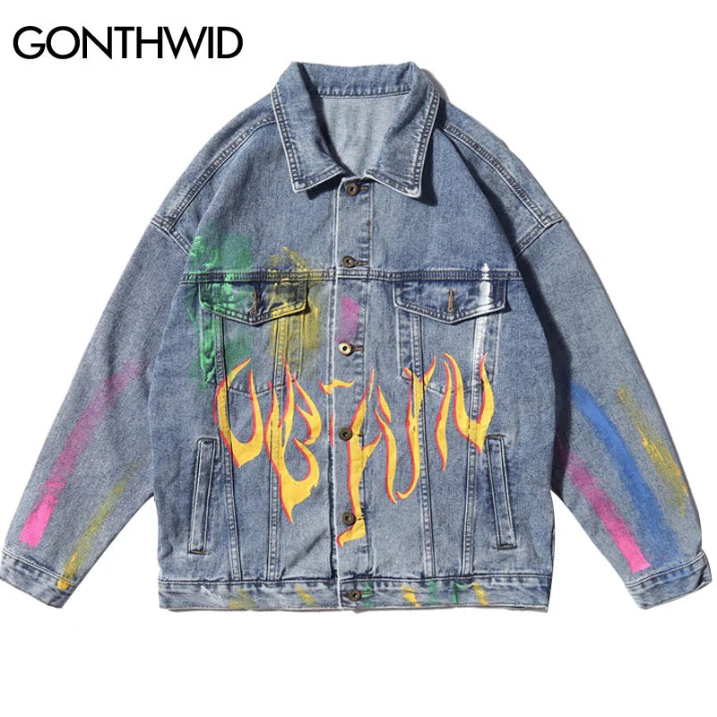 A light blue oversized denim jacket with a button-front closure, pointed collar, flap chest pockets, and side welt pockets. It features colorful paint-splatter accents and a bold flame graphic across the front for a graffiti-inspired streetwear look.