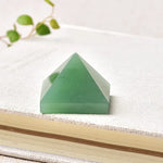 Small green pyramid-shaped gemstone or resin ornament resting on a textured book cover, with a blurred vine and leaves in the background.